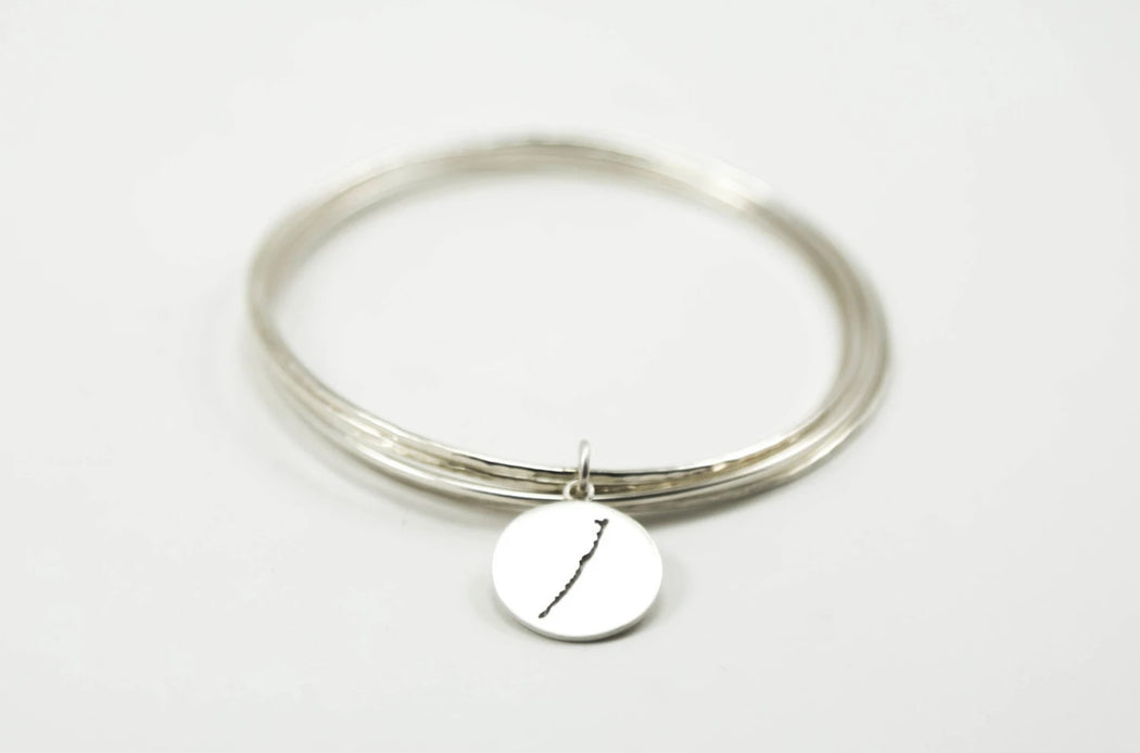 Stack of sterling silver hammered bangles featuring round Long Beach Island border with matte finish. 