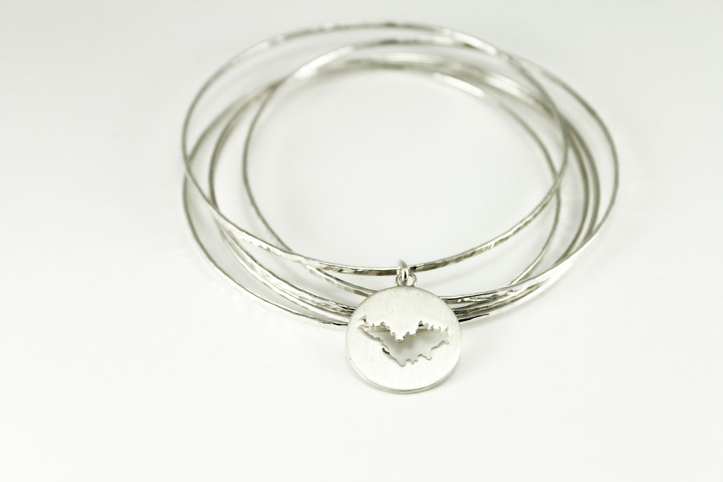 Stack of sterling silver hammered bangles featuring round St. Barth border with matte finish. 